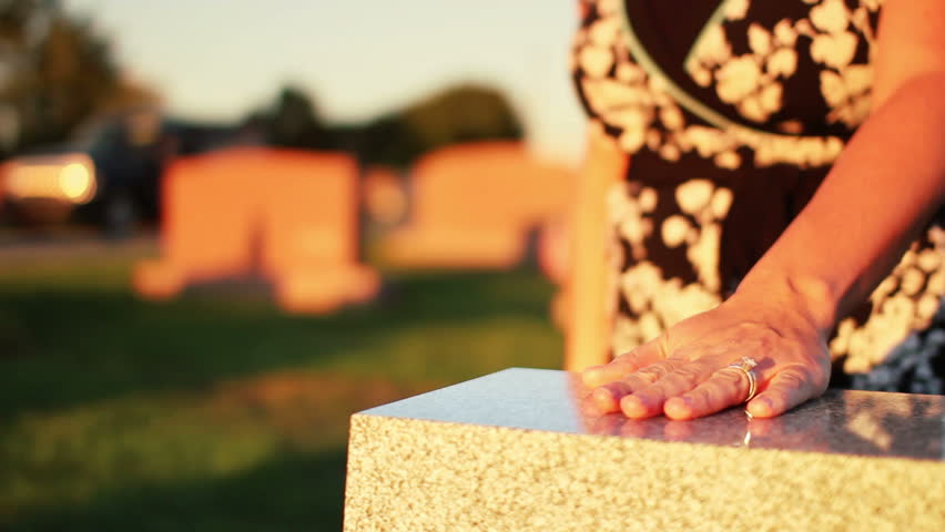 A woman visits a grave in a cemetery.