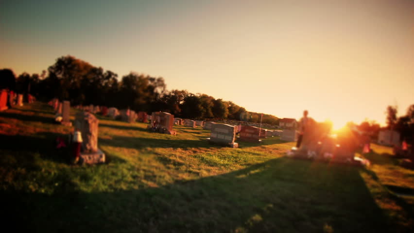 A woman visits a grave in a cemetery.