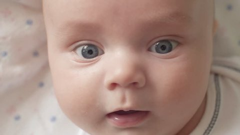 The look of the baby in the camera close up shot. A cute little baby is looking into the camera. The baby looks around and then smiles and laughs. Concept of caring for children, parental love and