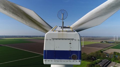 Aerial footage back of wind turbine blades turning also showing control housing and equipment on top of structure in further background showing more wind turbines producing sustainable energy 4k