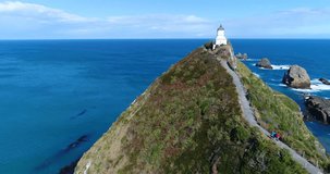 New Zealand tourists in nature landscape sightseeing at Nugget Point Lighthouse. Couple visiting Otago region and peninsula on South Island. Beautiful tourist destination and attraction from above