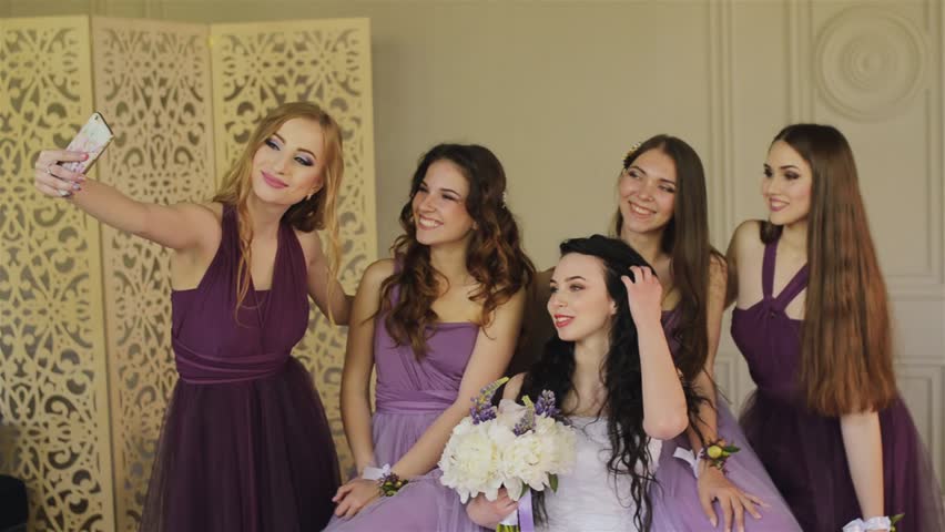 Bridesmaids taking a selfie on a smartphone and laugh during the morning of the bride in a beautiful photo studio. Beautiful girls in purple wedding dresses have fun in the studio. Royalty-Free Stock Footage #27801982