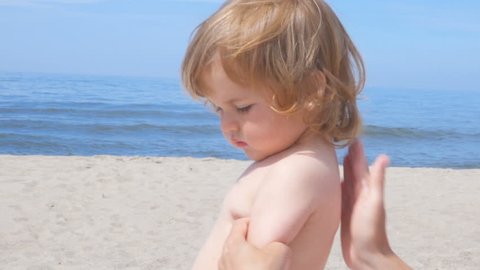 Mother applying sunscreen lotion on son back at beach. Mother preparing child for bath in sea. 