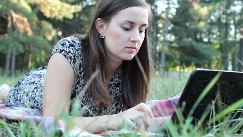 young girl lying on the grass and working on a laptop