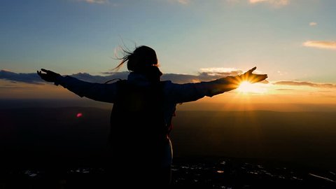 Young Active Successful Woman Raising Hands On Mountain Top. Woman Tourist with arms raised on top of mountain looking at sunset in Mountains. Hiker Hiking on top of a mountain. Healthy Lifestyle. 