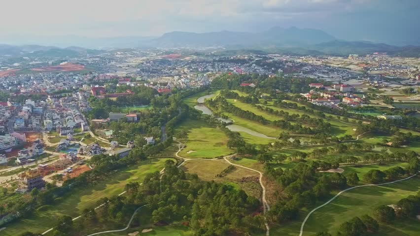 aerial view large green park with lawns trees and lakes among modern busy city and mountains in background