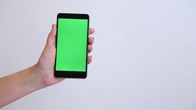 Close up of young caucasian female hands holding modern black smartphone with green touch screen isolated on white background. Woman flips through blank green pictures on phone with index finger. 