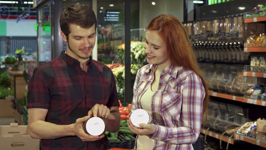 Attractive young couple arguing about the food composition data at the hypermarket. Handsome brunette man and his pretty redhead girlfriend pointing their forefingers on the can with some product