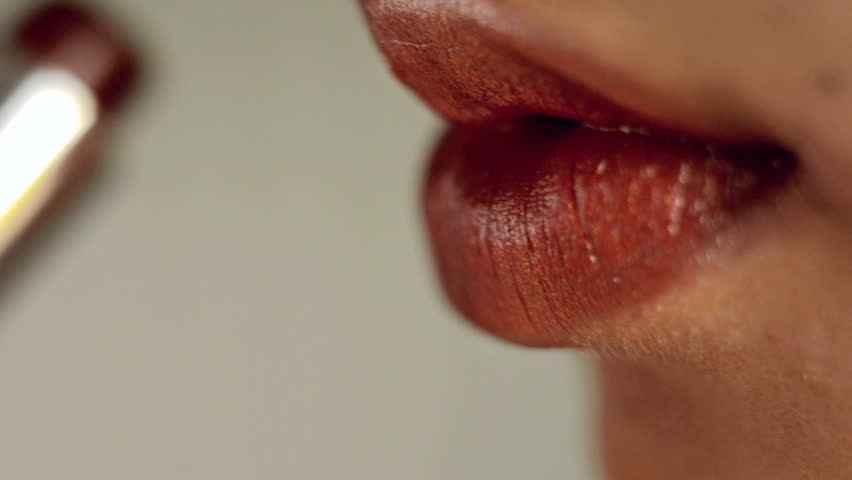 Close-up of a woman applying red lipstick on her lips.