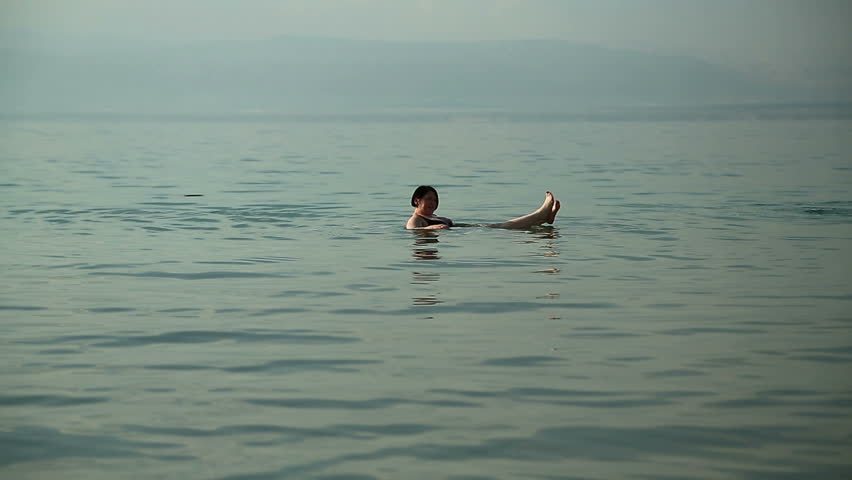 JORDAN, DEAD SEA, DECEMBER 8, 2016: Woman swim and relax in very salty water of Dead Sea, Hashemite Kingdom of Jordan. People swim in Dead Sea