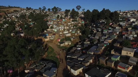 An aerial view of a township early one morning in Cape Town showing colourful zinc houses on a hill and african people heading off to work. 