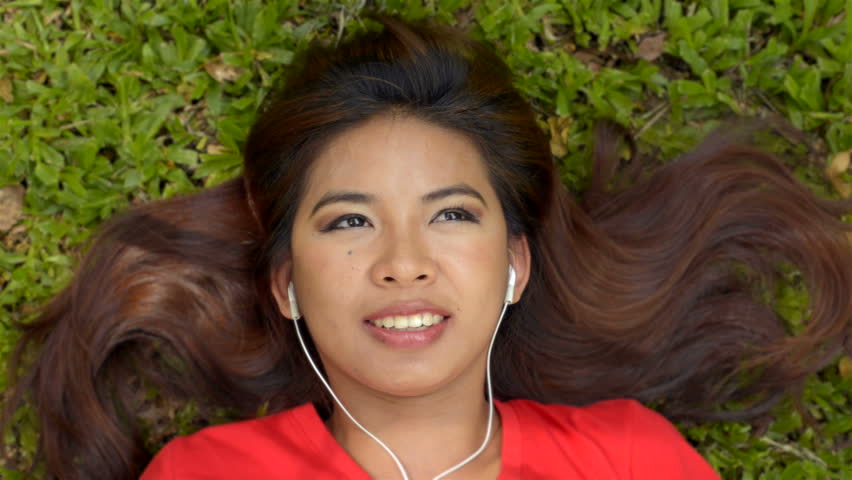 Young Asian woman lying on the grass in a park listening to music on her