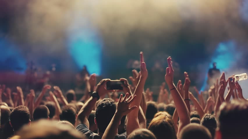 Iconic night rock concert front row crowd cheering hands in air slomo 100p.An outdoor summer night rock concert.People cheer move lift and clap their hands in unison against the strobing stage lights.