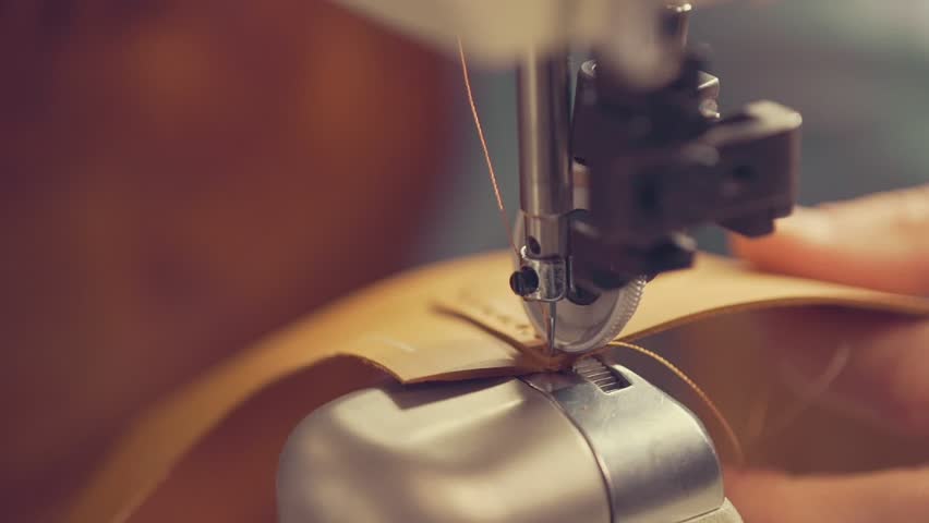 The master makes shoes in the workshop. Side view of using sewing machine to make seam