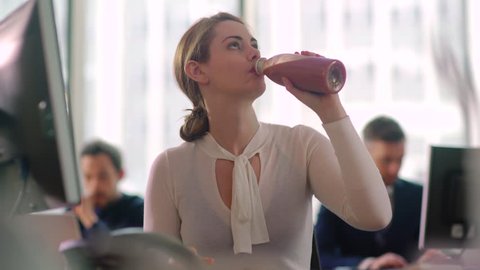 Woman sips a healthy smoothie drink whilst working at her desk. 