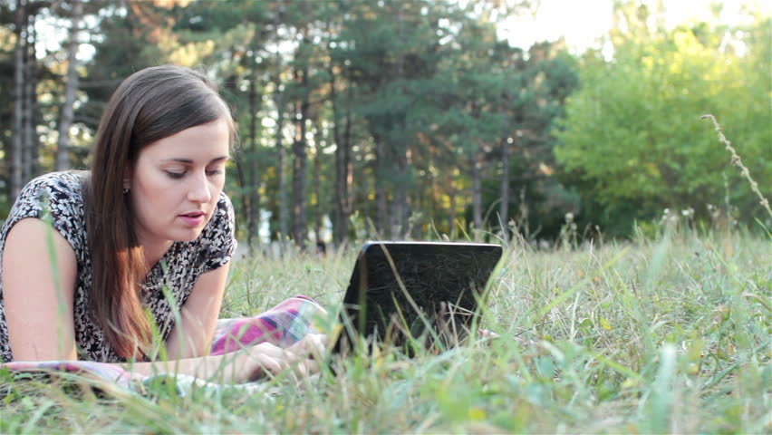 young woman lying on grass and using laptop