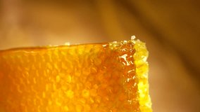 Honey dripping from honey dipper on honeycomb, over yellow background. Thick organic honey dipping from the wooden honey spoon. 4K UHD video footage. Ultra high definition 3840X2160 