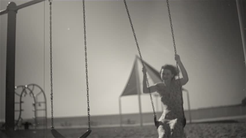 Young beautiful brunette woman is riding on a swing and smiling in retro style.