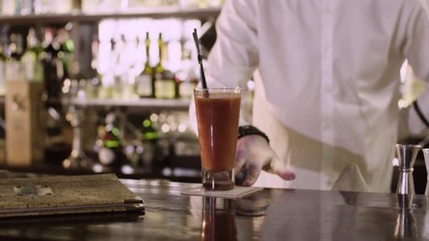 The barman in white shirt moves the finished bloody Mary to the edge of the bar counter close-up slow motion.