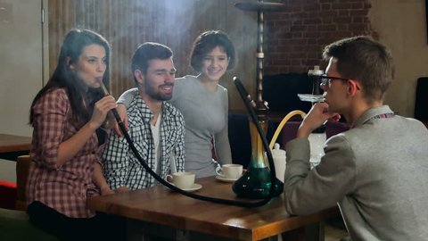 Young friends smoking hookah in shisha cafe