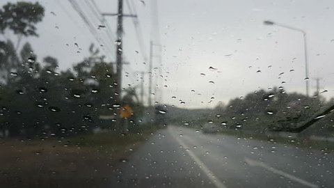 POV front driving a car or vehicle in the rain, focus on the rain at the windshield 