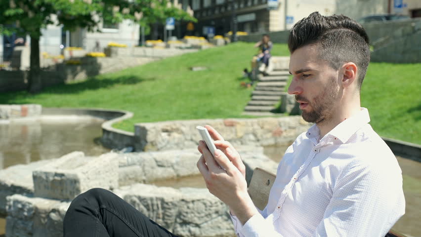 Handsome, elegant man sitting in the park and browsing internet on smartphone, steadycam shot

