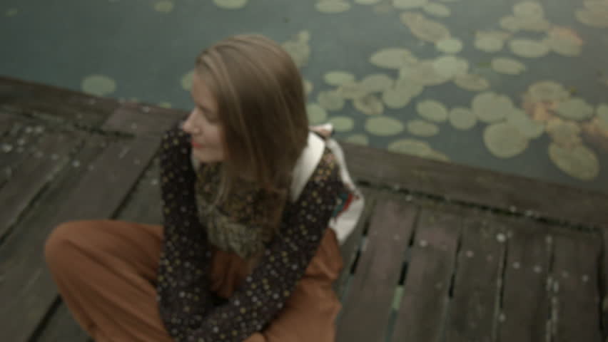 Young woman sitting near a lake on a wooden pier.