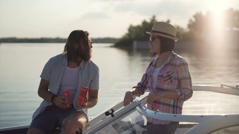 Young couple toasting each other with cans of beer as they relax in the evening on a lake in a motorboat while enjoying their summer vacation.