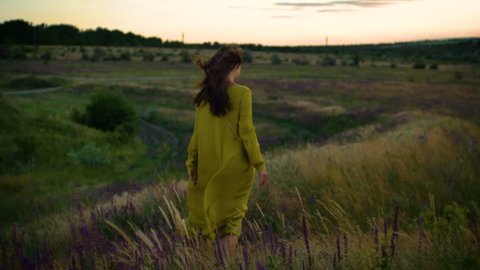 young woman walking on winded flowers field in sunset time