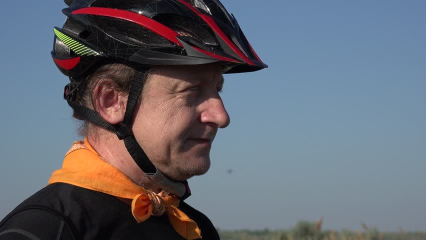 Close-up portrait male: Smiling biker tourist in helmet shoots panorama of summer landscape
