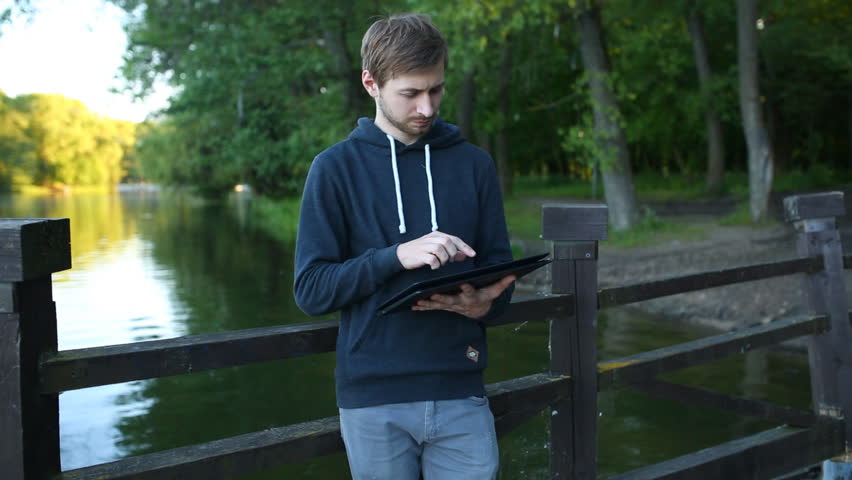 Man freelancer working on the lake with a tablet computer, image at sunset. The lights of a sun.
