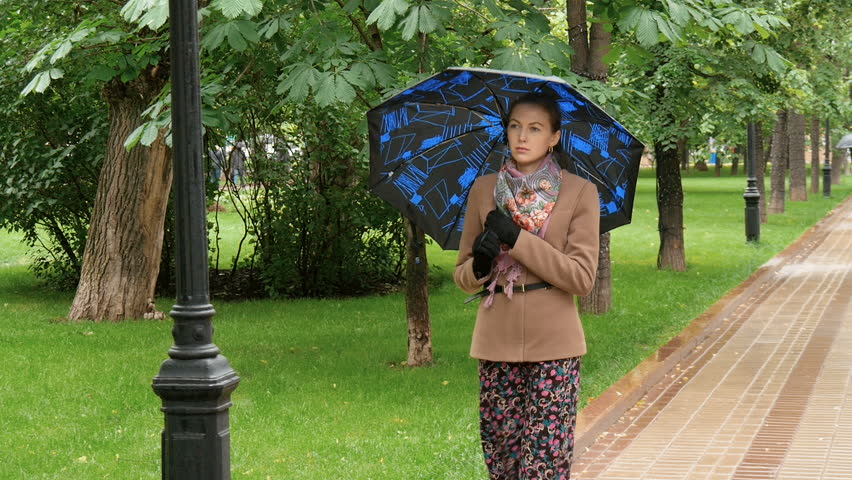 Young sad woman is walking in the rain in the park.