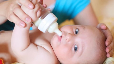 mother feeds with milk of small child from small bottle in hands