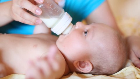 small child drinks milk from small bottle in hands of mother lying on back