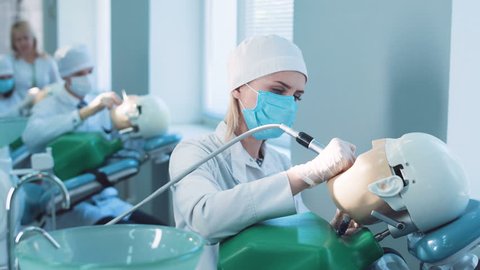 Dentistry student or hygienist practicing on a dummy at a medical school as a qualified teacher demonstrates the technique to her from behind