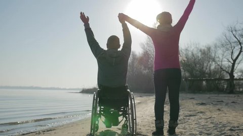 disabled and girl raise their hands to top, handicapped person gives hand to girlfriend, back view