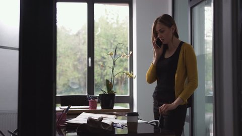 Young designer attractive woman standing, thinking on a new project and speaking on the phone in the office