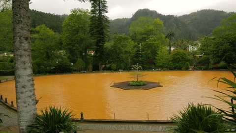 Panning shot of yellow iron water heated thermal pool in the edenic Parque Terra Nostra, Furnas, Sao Miguel, The Azores, Portugal.