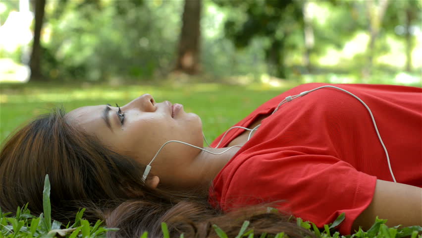 Young Asian woman listening to music on her headphones, while relaxing lying on