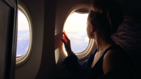 A young girl travels by plane and sits by the window and enjoys the view and then closes the porthole. 1080p