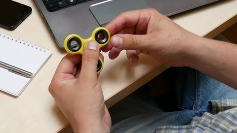 Manager on the Workplace in the Office Plays and Twists the Yellow Plastic Hand Spinner, Relaxing during the Working Day. Toy for Increased Focus And Stress Relief. Hand Finger Spinner Spins