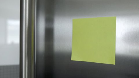 Yellow post it note on a fridge. Tracking in and angle.