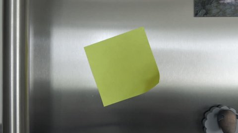 Yellow post it note on a fridge. The note is in an angle. Tracking in shot.