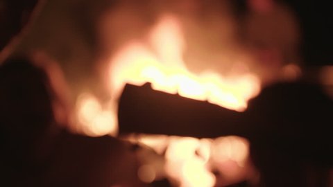 Guitar stems silhouetted by a campfire as two men play and sing songs with a group of friends while camping outside in nature. Night time exterior friends and family static shot with people.