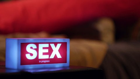 woman approaching man in bed sex sign in foreground 
