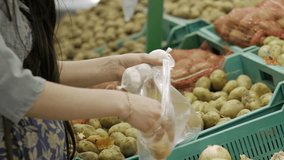 Pregnant young woman put onion in the transparent plastic packing bag. Women hands closeup. Shopping and people concept. Stock video footage.