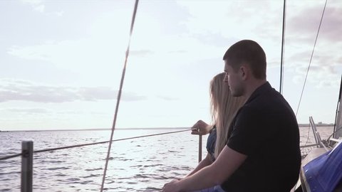 Romantic time of girl and boy on the nature together. The girl with the young man sit on the white yacht having lowered legs from edge of the yacht