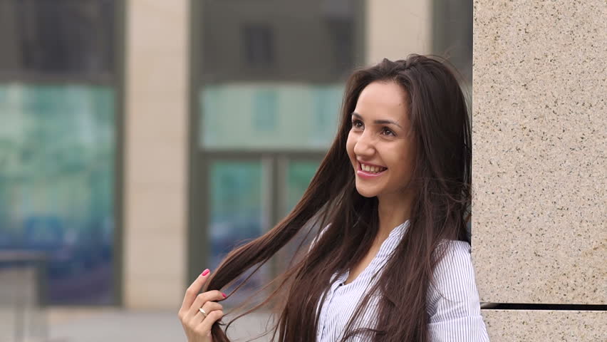 Young happy girl with luxurious long hair is leaning on wall and smiling.
