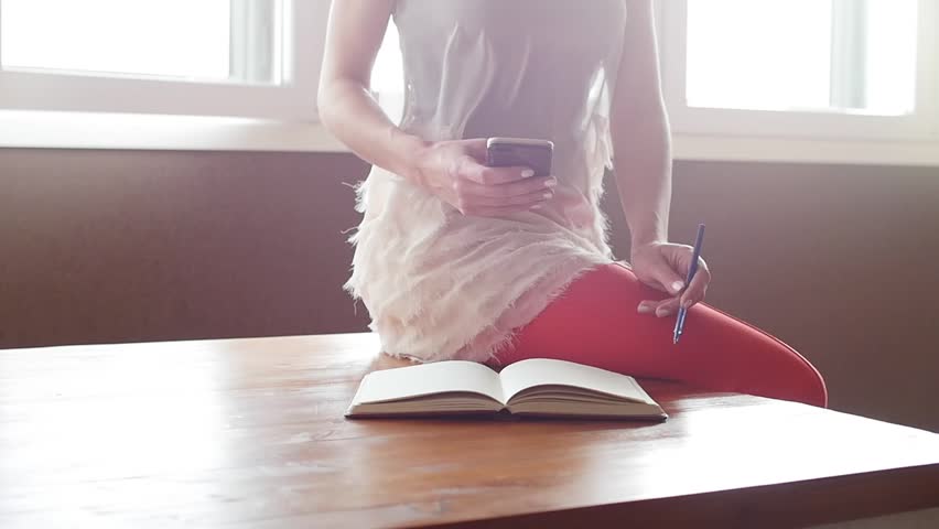 Hands of woman writing in her diary and using a smart phone