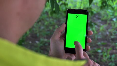 Closeup of male hands holding smartphone with green screen-prekeyed effects.nature in the background.